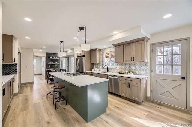 kitchen with appliances with stainless steel finishes, sink, hanging light fixtures, a center island, and light hardwood / wood-style floors