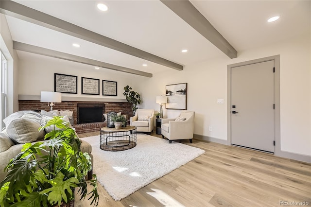 living room featuring beam ceiling, light hardwood / wood-style floors, and a brick fireplace