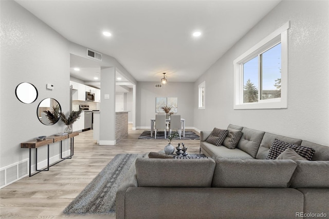 living room featuring baseboards, light wood-style flooring, visible vents, and recessed lighting