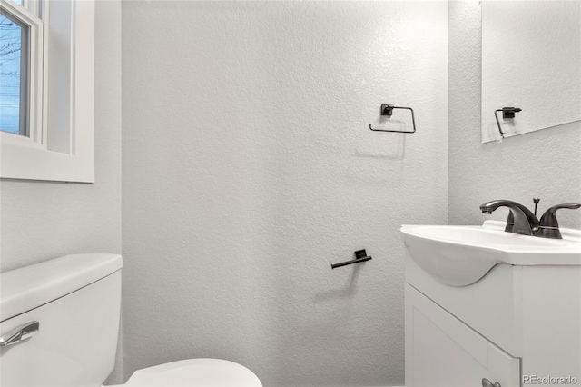 bathroom featuring a textured wall, vanity, and toilet