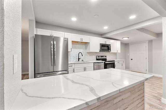 kitchen with light stone counters, stainless steel appliances, decorative backsplash, white cabinets, and a sink