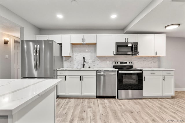 kitchen with white cabinets, appliances with stainless steel finishes, light stone countertops, light wood-type flooring, and a sink