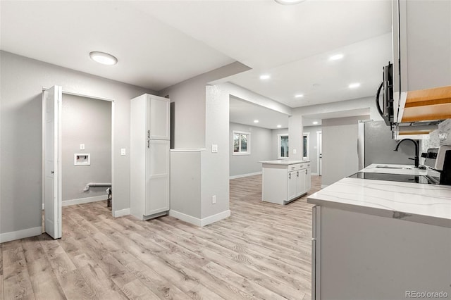 kitchen with baseboards, white cabinets, light wood-style flooring, stainless steel microwave, and light stone countertops