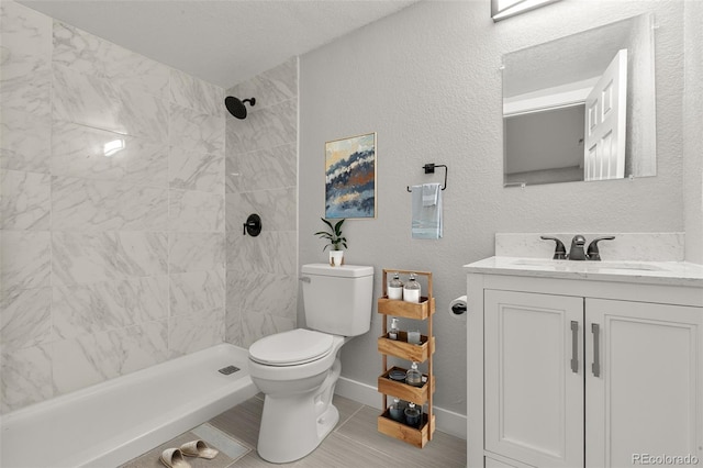 bathroom with baseboards, tiled shower, a textured wall, toilet, and vanity