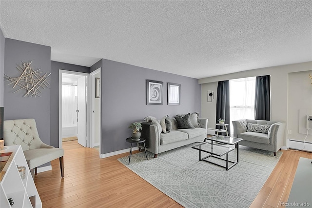 living area featuring baseboard heating, baseboards, a textured ceiling, and light wood finished floors