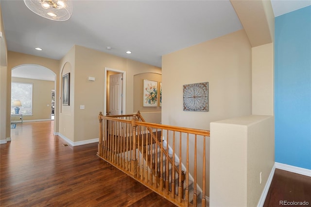 hall with an upstairs landing, wood finished floors, arched walkways, recessed lighting, and baseboards