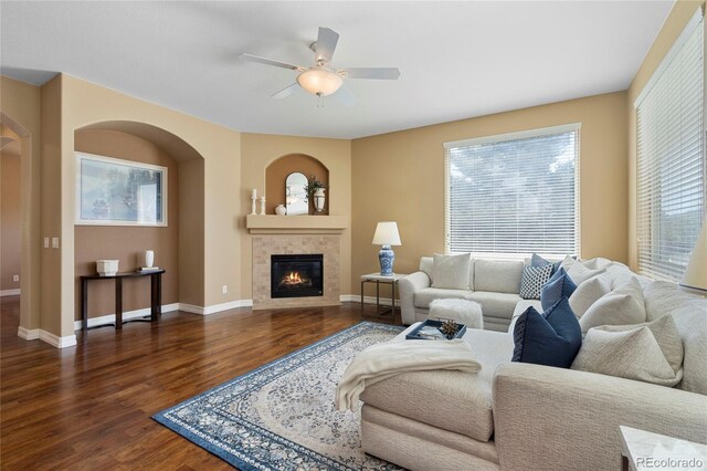 living area featuring wood finished floors, ceiling fan, baseboards, and arched walkways
