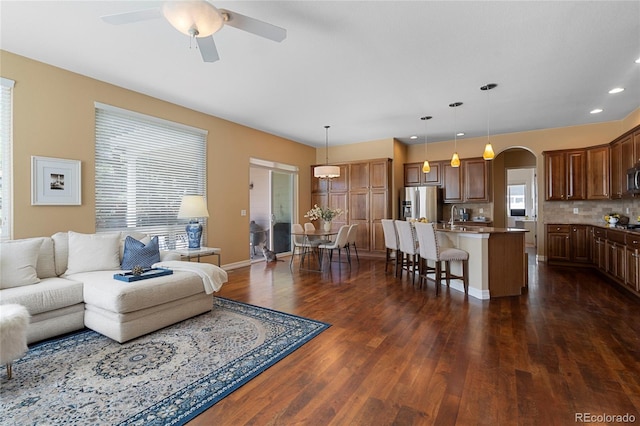 living room featuring dark wood-style flooring, arched walkways, recessed lighting, a ceiling fan, and baseboards