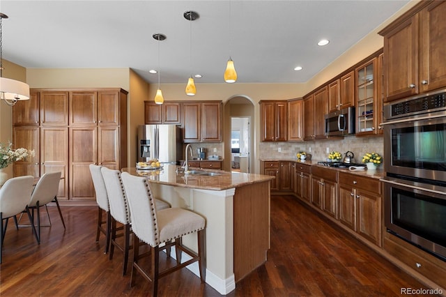 kitchen featuring stainless steel appliances, a sink, light stone countertops, brown cabinetry, and recessed lighting