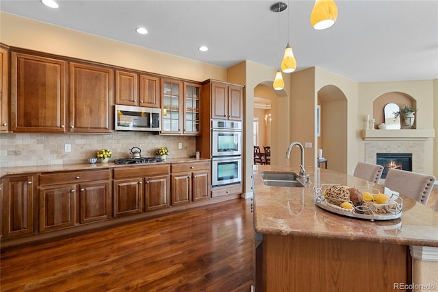kitchen featuring a sink, stainless steel appliances, dark wood-style flooring, light stone counters, and brown cabinetry