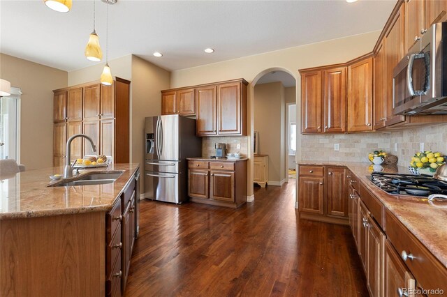 kitchen with stainless steel appliances, a sink, brown cabinets, dark wood finished floors, and recessed lighting