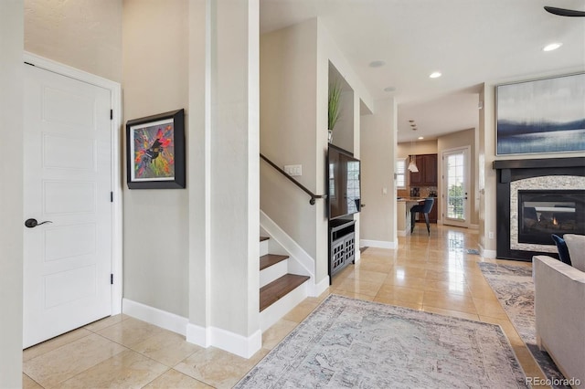 foyer entrance with baseboards, a glass covered fireplace, light tile patterned floors, and stairway