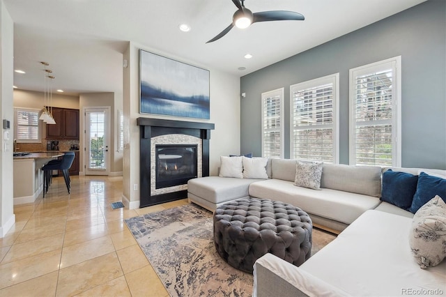 living room featuring ceiling fan, a glass covered fireplace, recessed lighting, baseboards, and light tile patterned floors