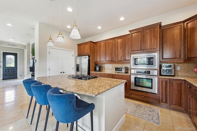 kitchen featuring a kitchen island, tasteful backsplash, light stone counters, light tile patterned floors, and stainless steel appliances