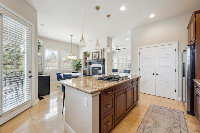 kitchen featuring a glass covered fireplace, open floor plan, a center island, appliances with stainless steel finishes, and light tile patterned floors
