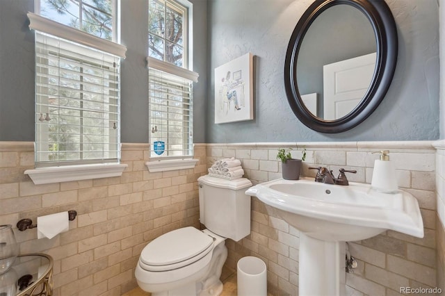 bathroom with tile walls, a wainscoted wall, and toilet
