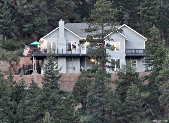 83 Wilderness Cornerstone Rd, Evergreen, CO 80439 - view of front facade featuring a chimney, a view of trees, a balcony, and stairway