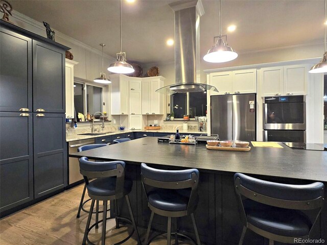 83 Wilderness Cornerstone Rd, Evergreen, CO 80439 - kitchen with appliances with stainless steel finishes, island exhaust hood, a sink, a kitchen bar, and ornamental molding
