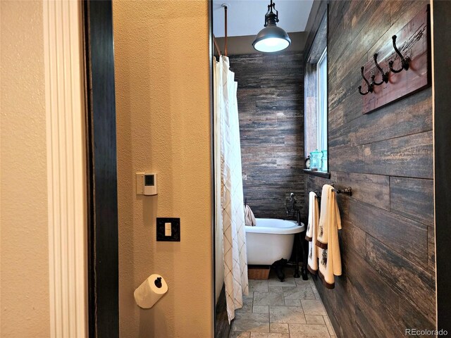 83 Wilderness Cornerstone Rd, Evergreen, CO 80439 - bathroom with stone tile flooring, a textured wall, a freestanding bath, and wooden walls