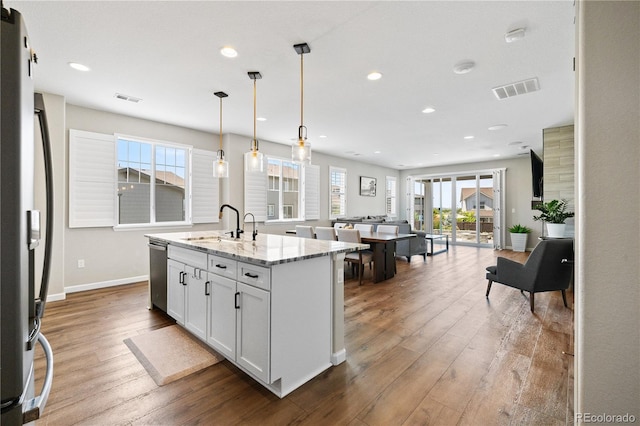 1925 Peregrine Dr, Brighton, CO 80601 - kitchen featuring appliances with stainless steel finishes, an island with sink, hardwood / wood-style floors, recessed lighting, and light stone countertops