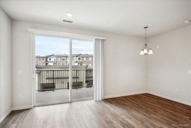 unfurnished room featuring baseboards, a notable chandelier, visible vents, and wood finished floors