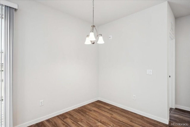 empty room featuring dark wood finished floors, a chandelier, and baseboards