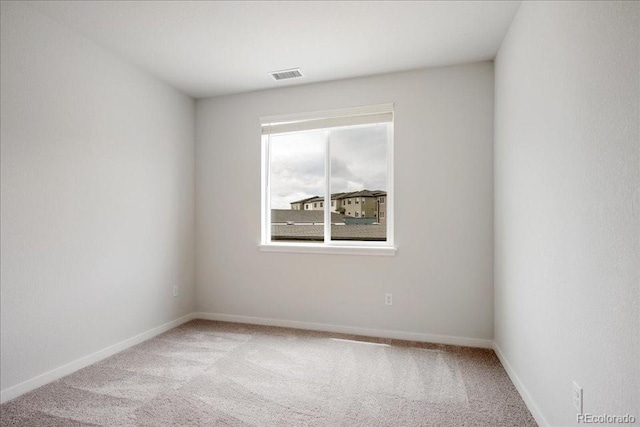 empty room featuring baseboards, light carpet, and visible vents