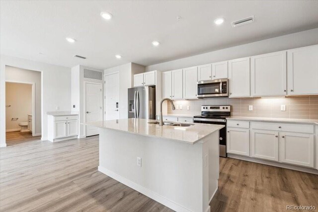 485 Interlocken Blvd Unit 209, Broomfield, CO 80021 - kitchen with stainless steel appliances, a sink, light wood-style flooring, decorative backsplash, and white cabinetry