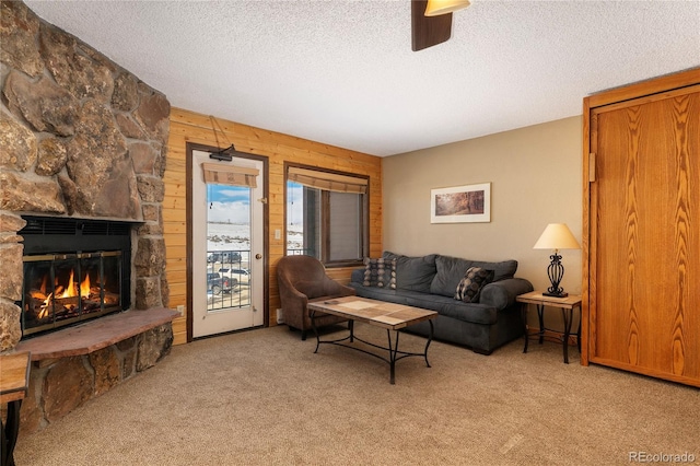 living room with light carpet, wood walls, a stone fireplace, and a textured ceiling