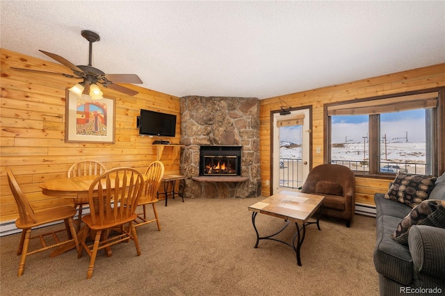 living area featuring wooden walls, carpet, a stone fireplace, and a baseboard radiator