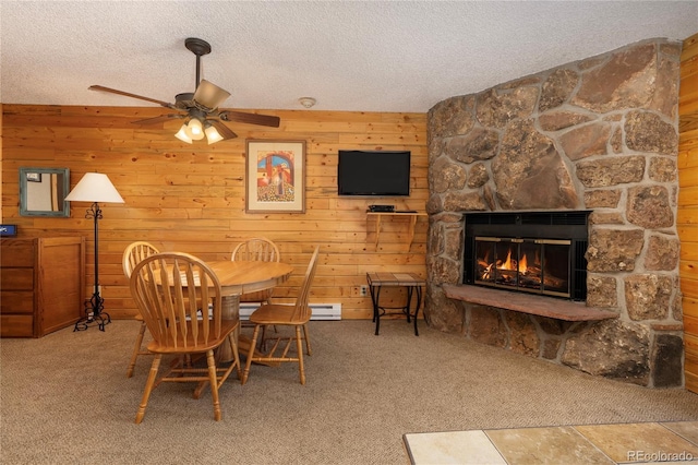 dining room featuring a textured ceiling, a stone fireplace, wood walls, and carpet flooring