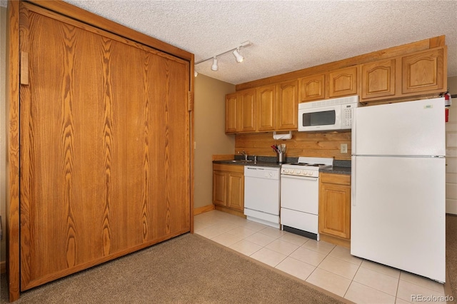 kitchen with light tile patterned floors, white appliances, a textured ceiling, and brown cabinetry