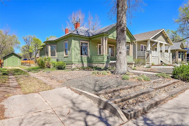 view of front of home with a chimney, an outdoor structure, a porch, and a storage unit