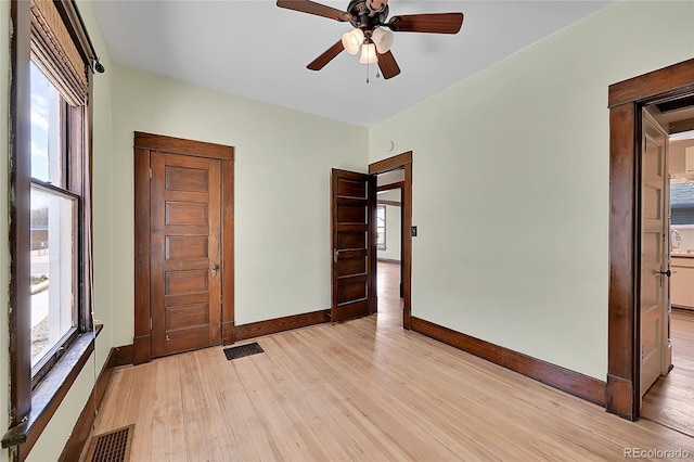 empty room featuring light wood-type flooring, baseboards, visible vents, and ceiling fan