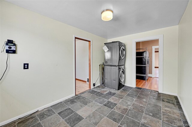 empty room with stacked washer and clothes dryer, stone tile floors, and baseboards