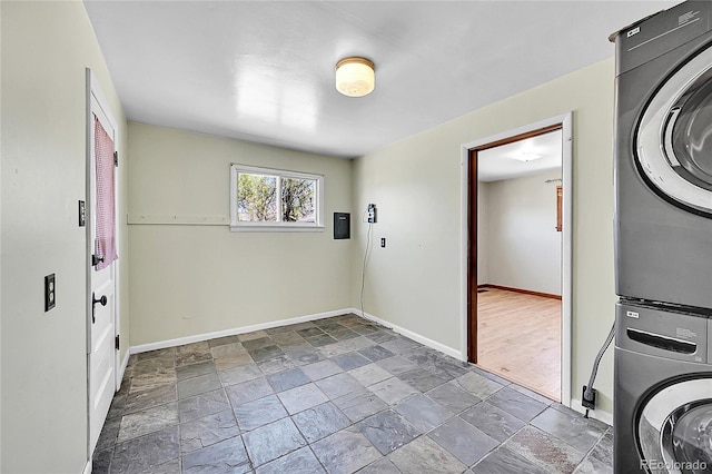 laundry area with stone tile floors, baseboards, stacked washer and clothes dryer, and laundry area