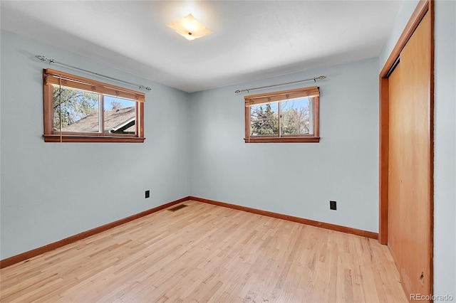 unfurnished bedroom featuring light wood-style flooring, a closet, baseboards, and multiple windows