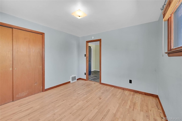 unfurnished bedroom featuring baseboards, light wood finished floors, visible vents, and a closet
