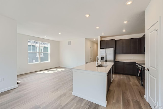 kitchen with black range with electric stovetop, sink, stainless steel fridge, light hardwood / wood-style floors, and a kitchen island with sink