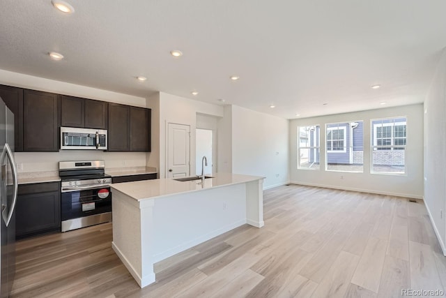 kitchen with dark brown cabinetry, stainless steel appliances, sink, light hardwood / wood-style flooring, and an island with sink