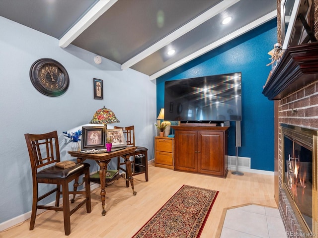 interior space with lofted ceiling with beams, a brick fireplace, and light wood-type flooring