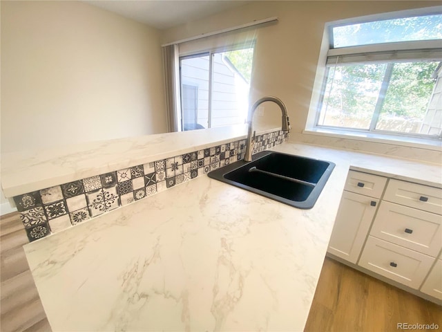 kitchen featuring light wood-type flooring, white cabinets, light stone counters, and sink