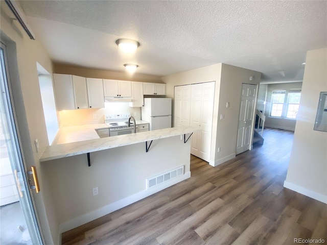 kitchen with white cabinetry, a kitchen bar, kitchen peninsula, white appliances, and dark hardwood / wood-style flooring