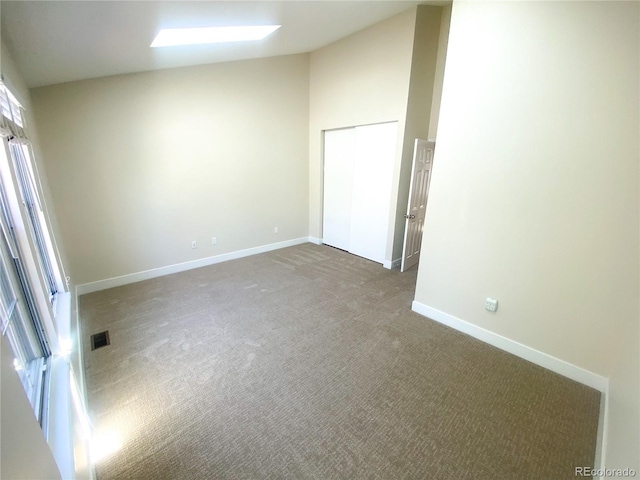 spare room with vaulted ceiling with skylight and dark carpet