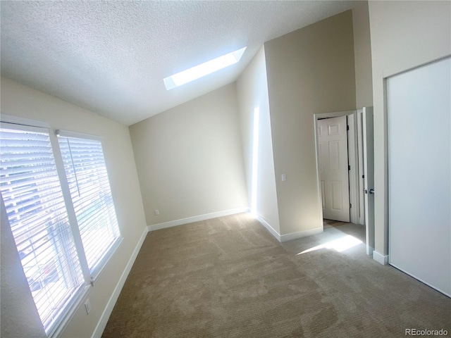 carpeted spare room with a textured ceiling and vaulted ceiling with skylight