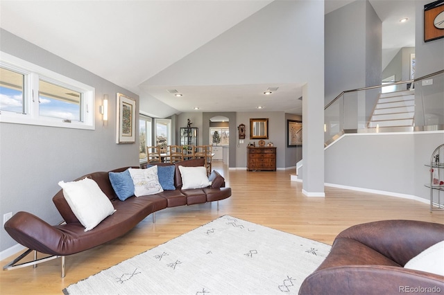 living area featuring stairway, high vaulted ceiling, baseboards, and wood finished floors