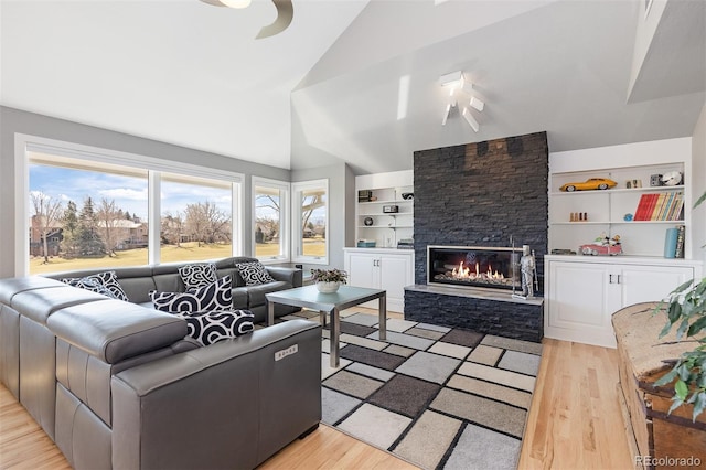 living room featuring a stone fireplace, lofted ceiling, built in features, and light wood-style floors