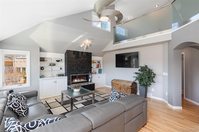 living room featuring ceiling fan, light wood-type flooring, arched walkways, and a large fireplace