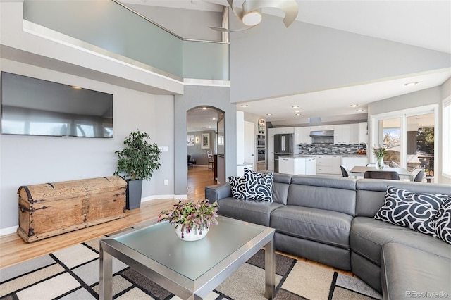 living area with light wood-type flooring, high vaulted ceiling, recessed lighting, arched walkways, and baseboards