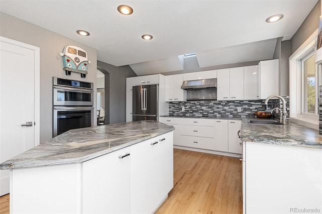 kitchen featuring a sink, a kitchen island, range hood, stainless steel appliances, and arched walkways